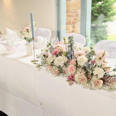 Aufwendig gestalteter Brauttisch mit länglichem Gesteck in Pastelltönen – florale Prinzessinnenhochzeit von Pfirsichkoeppchen Weddings.